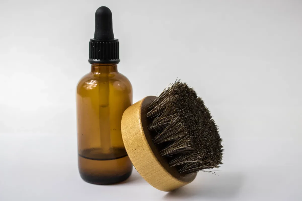 A small bottle of beard oil beside a shaving brush and comb