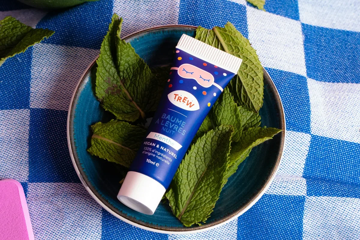 A tube of lip balm beside fresh mint leaves