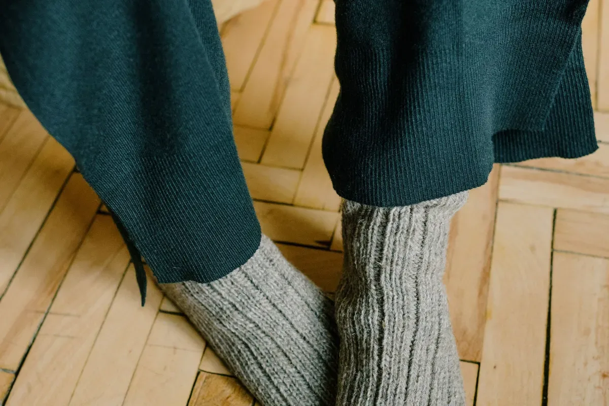 Wool knit socks on someone's feet, standing on a wooden floor